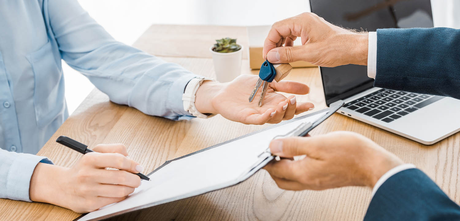 Person handing real estate property keys to another person as they sign paperwork after a home inspection 